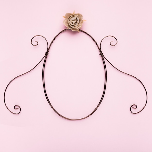 Free photo oval shape frame with artificial rose on pink backdrop