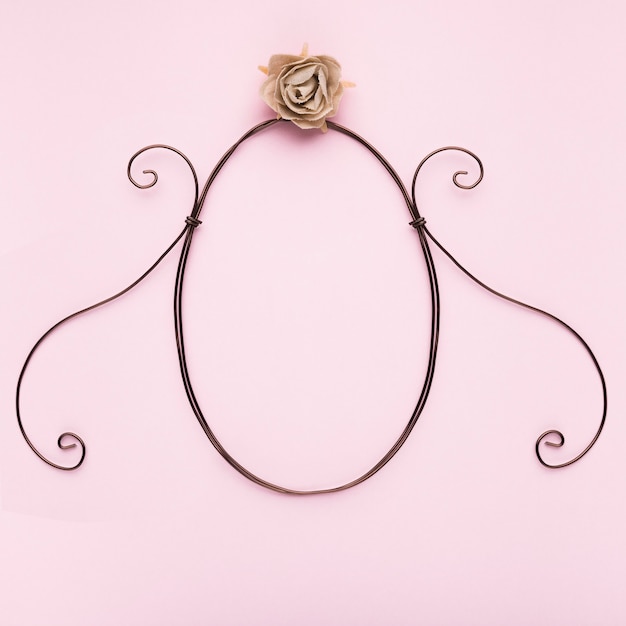 Oval shape frame with artificial rose on pink backdrop