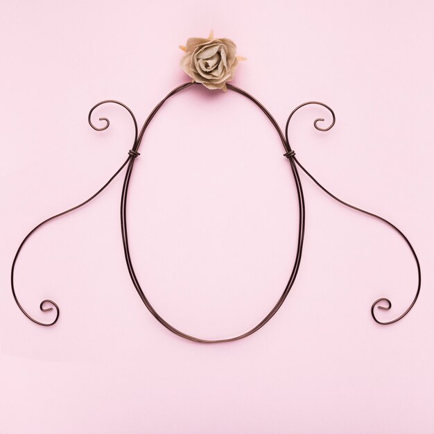 Oval shape frame with artificial rose on pink backdrop