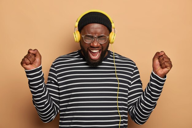 Overemotive black man dances with raised fists, wears headphones on ears