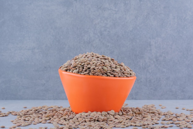 Overfilled bowl nested in a scattered pile of brown lentil on marble surface