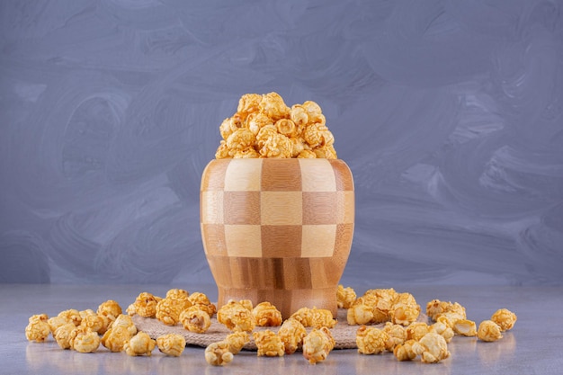 Overfilled, checkered bowl surrounded by scattered caramel popcorn on marble background. High quality photo