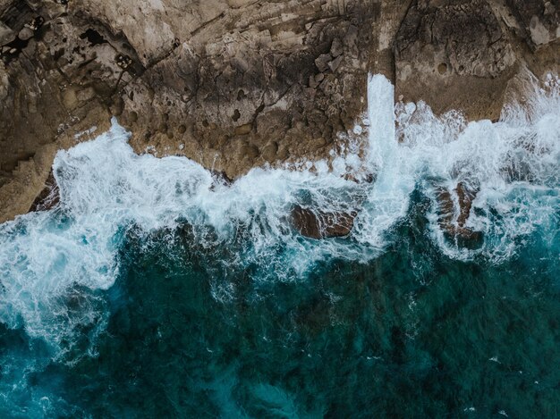 Overhead aerial shot of the beautiful ocean cliffs and the water splashing on them