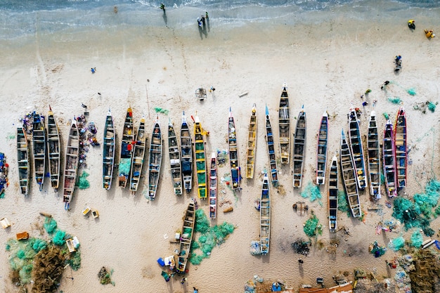 Overhead aerial shot of different colored boats on a sandy beach with the sea nearby