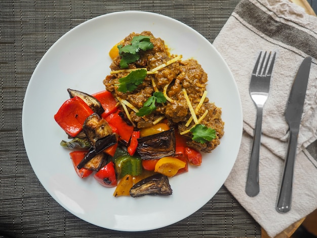 Overhead closeup shot of middle eastern cooked food on a white plate with a fork and a kitchen knife