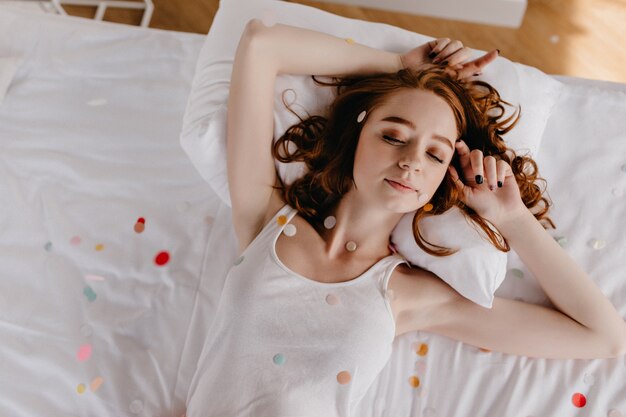 Накладные портрет женщины имбиря с модным макияжем на кровати. Удивительная расслабленная девушка в пижаме, лежащая в спальне.