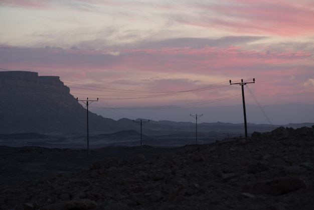 Overhead power lines in the valley under the cloudy sunset sky