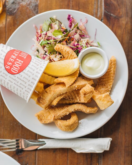 Overhead selective closeup shot of a vegetable salad, fish chips and mayonnaise on a white plate