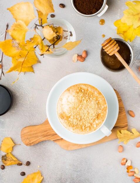 Overhead shot of coffee with nuts in a white ceramic cup on a table with a bowl of honey and dipper