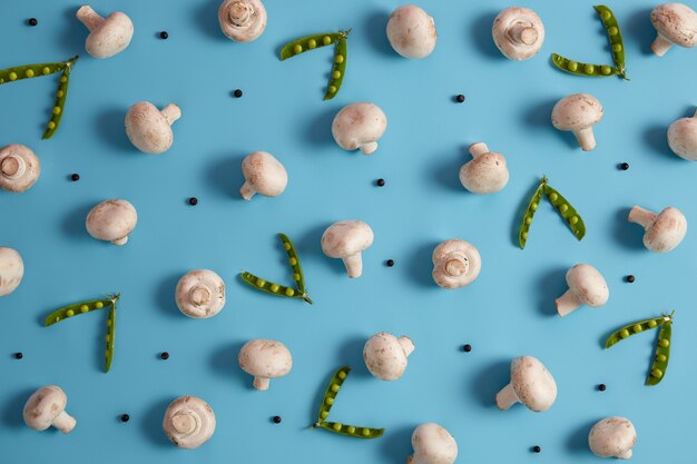 Overhead shot of edible mushrooms, ripe green peas and peppercorns isolated on blue background. Vegetables for preparing delicious soup. Template for menu or poster. Ingredients for cooking.