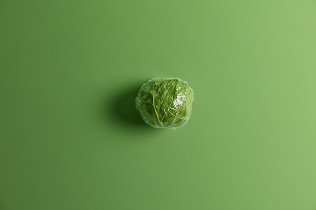 Overhead shot of green cabbage wrapped in clear plastic food film ready for consumption. Healthy organic product collected from garden or field. Rich harvest, gardening and agriculture concept.