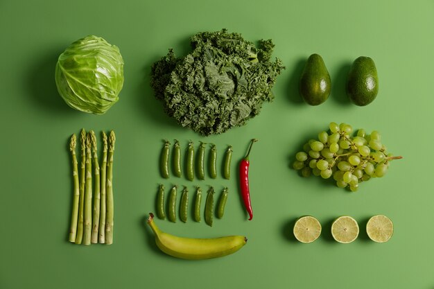 あなたの健康的な栄養のための緑の果物と野菜のオーバーヘッドショット。キャベツ、アスパラガス、アボカド、エンドウ豆、バナナ、ライム、赤唐辛子、ブドウ。食べる有機食材のコレクション