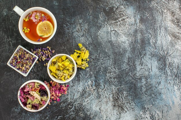 Overhead shot of herbal tea near bowls of dry flowers on grey ground