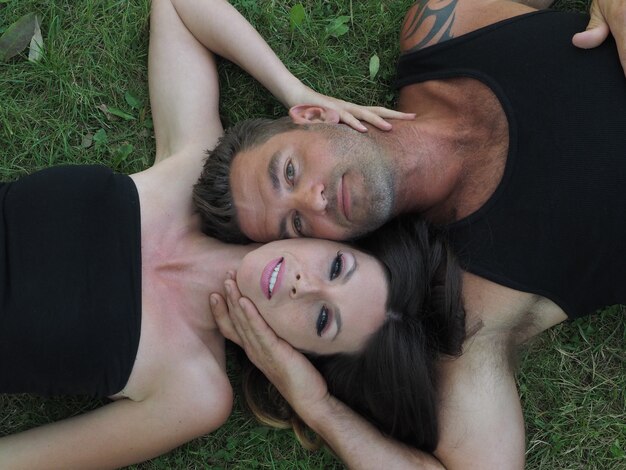 Overhead shot of a male and a female lying on the grass cheek to cheek