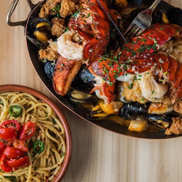 Overhead shot of pasta near a pan of fried lobster and meat with oysters on a wooden surface