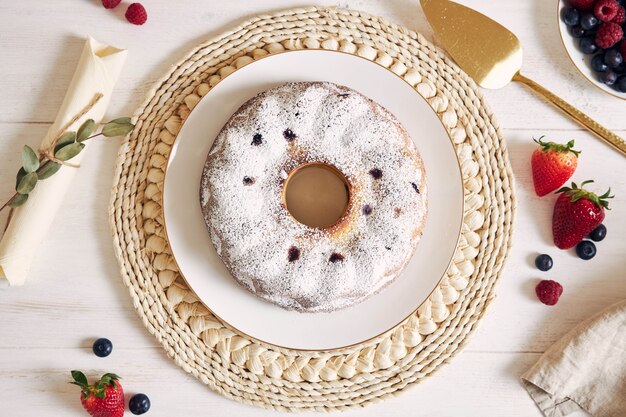 Overhead shot of a ring cake with fruits and powder on a white table with white background