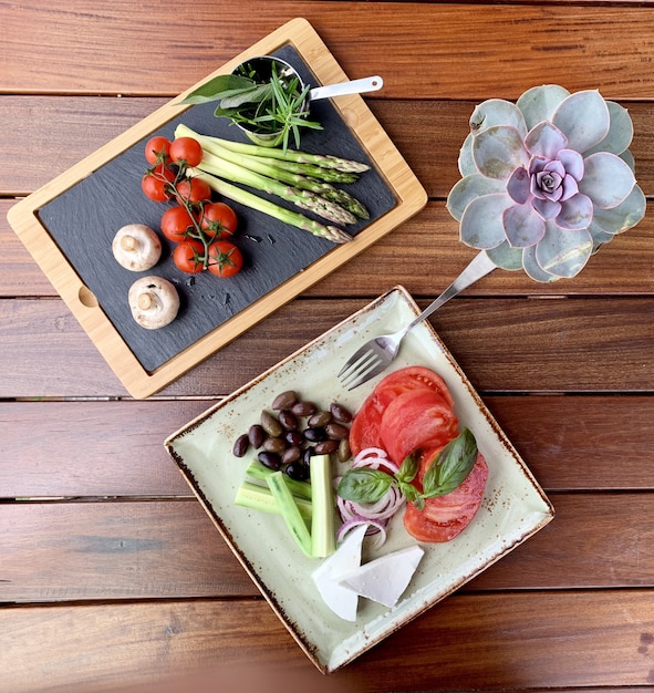 Overhead shot of salad with beans and cheese on a plate near a wooden tray with vegetable near  rose