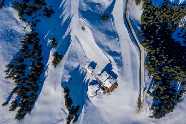 Overhead shot of small houses on a snowy mountain surrounded by trees during daylight