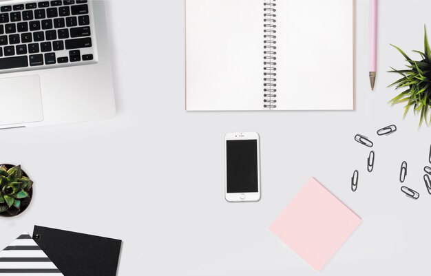 노트북, 분홍색 스티커 메모 및 종이 클립 흰색 책상에 스마트 폰의 오버 헤드 샷