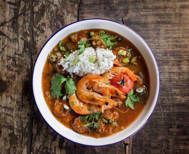 Overhead shot of soup with shrimp and vegetable leaves in a bowl on a wooden surface