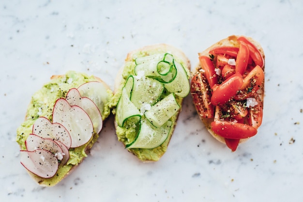 Overhead shot of three delicious sandwiches with avocado sauce on a marble background