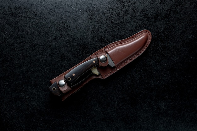 Free photo overhead shot of two fixed knives with brown handle in a brown case on black table