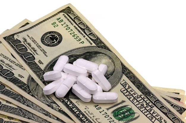 Overhead shot of white tablets placed at the top of a dollar bill with a white background