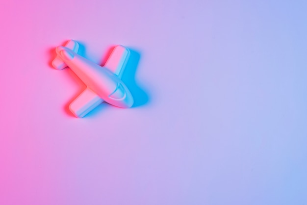 An overhead view of airplane with blue shadow against pink background