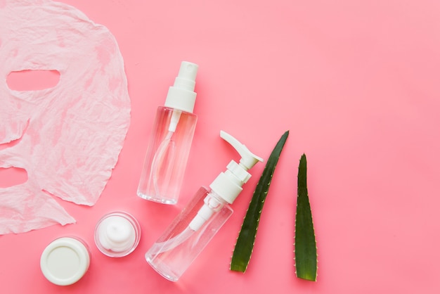 An overhead view of aloevera spray bottle and moisturizer cream on pink background