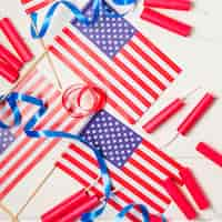 Free photo an overhead view of american flags with ribbons and firecracker on white desk