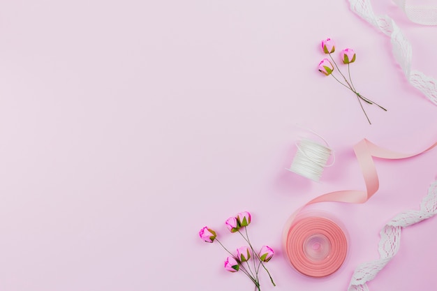 An overhead view of artificial roses; spool and ribbons on pink background