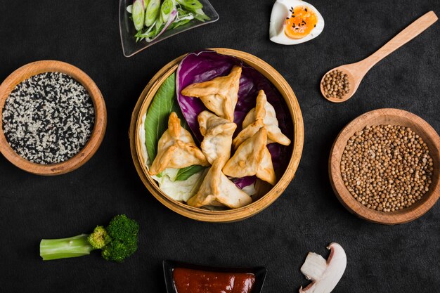 An overhead view of asian style dumplings with sesame and coriander seeds on black background