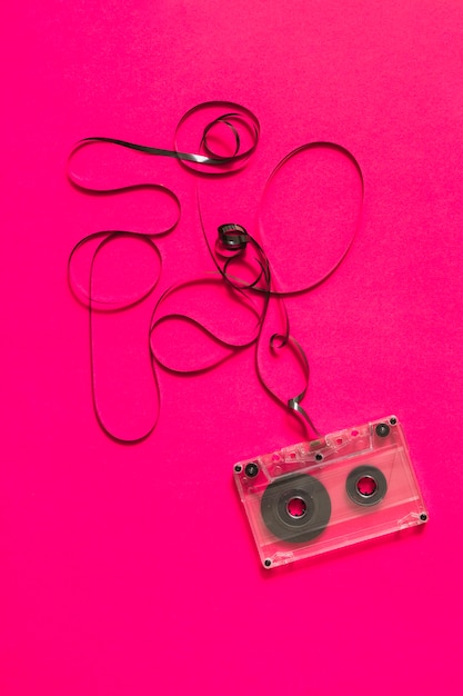 An overhead view of audio cassette with tangled tape on pink background