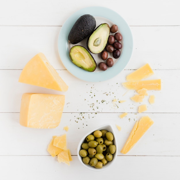 An overhead view of avocado; olives and cheese chunk on white table