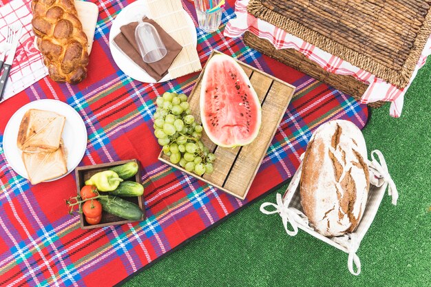 An overhead view of baked bread; fruits and picnic basket on blanket