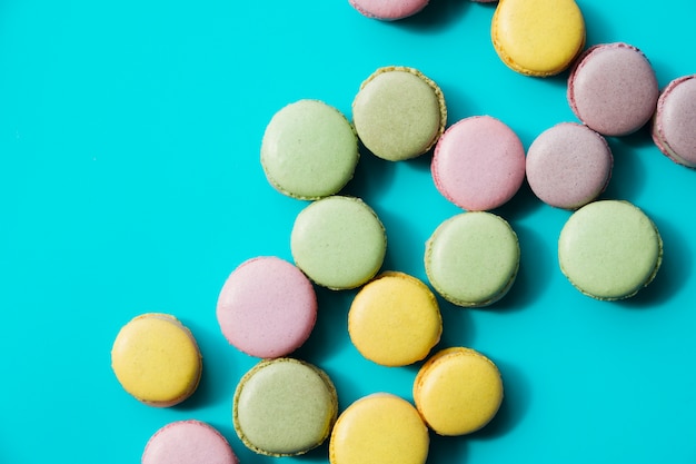 An overhead view of baked green; yellow and pink macaroons on blue background