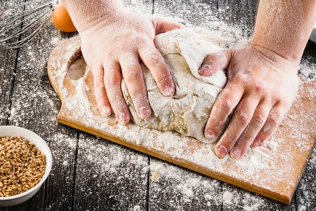 Overhead view of baker's hand preparing dough with flour on chopping board