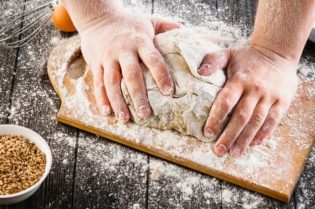 Верхний вид руки пекаря, готовящего тесто с мукой на разделочной доске