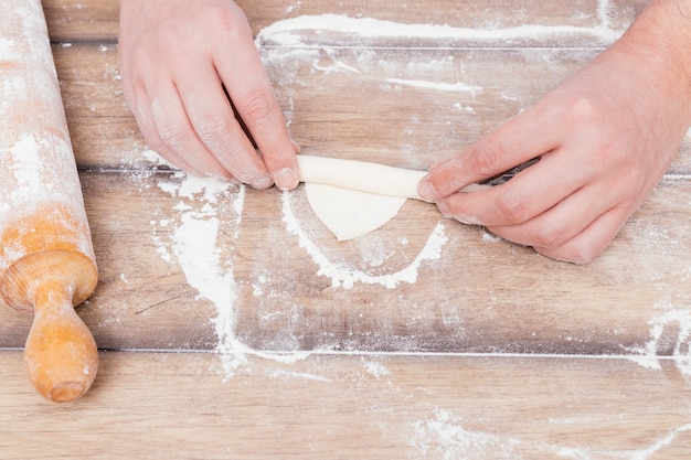 An overhead view of a baker's hand rolling the dough on flour over the table