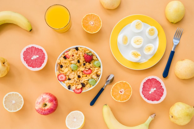 Free photo an overhead view of banana; grapefruit; orange; pears; juice; boiled eggs and cornflakes on brown background