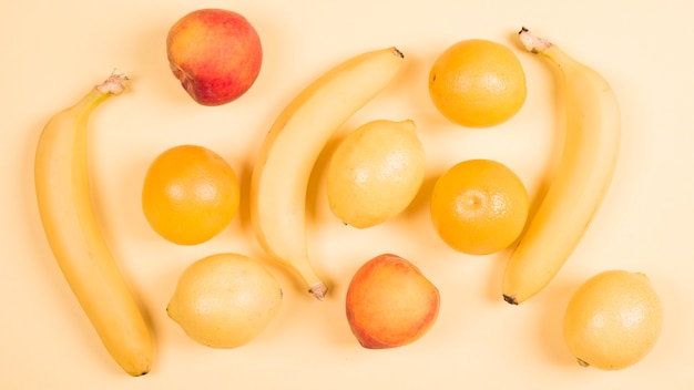 An overhead view of banana; peach; apple; oranges and lemons against beige background