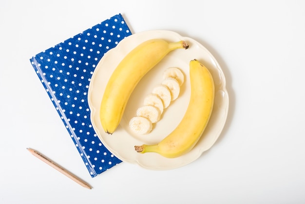 Overhead view of bananas; pencil and notebook on white surface