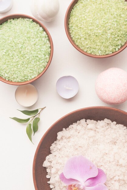 Overhead view of bath salt bowls with candle and spa bomb on white background