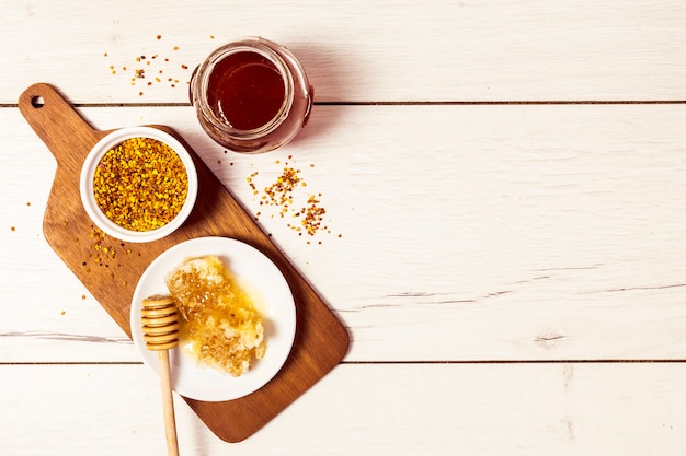 Free photo overhead view of bee pollen; honeycomb and honey on white wooden textured