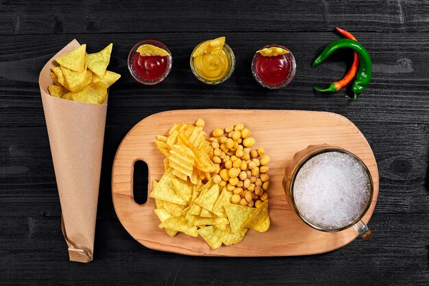 Overhead view of beer glass and snacks with sauce on black wooden table.