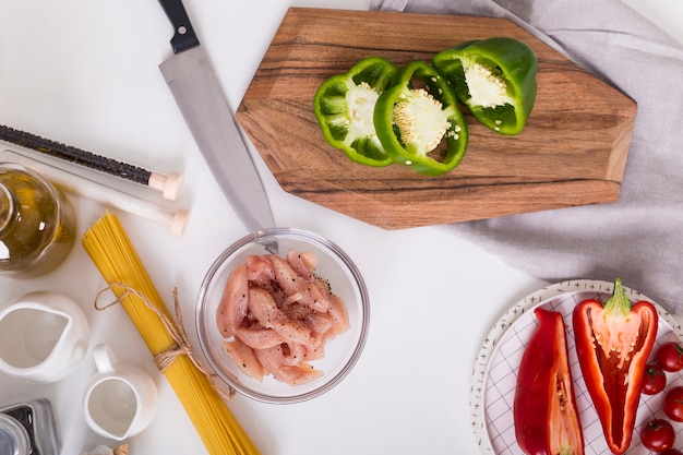 An overhead view of bell peppers; sliced chicken; spaghetti on white backdrop