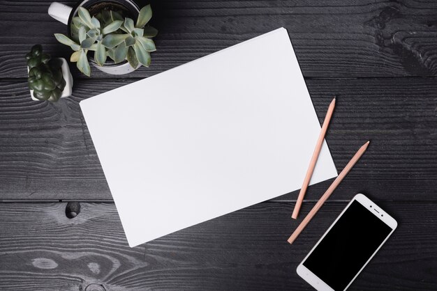 An overhead view of blank paper with two colored pencils and smartphone on wooden table