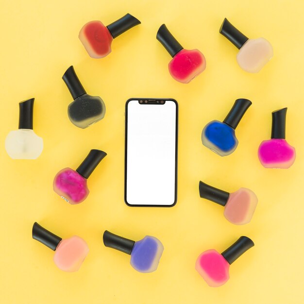 An overhead view of blank screen smartphone with colorful nail varnish on yellow background