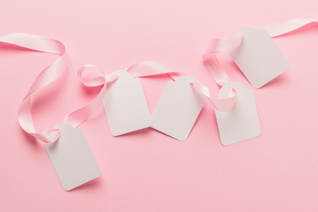 Overhead view of blank tags and pink ribbon against plain pink backdrop