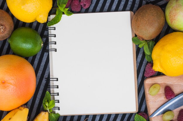 An overhead view of blank white spiral notepad with various fresh fruits